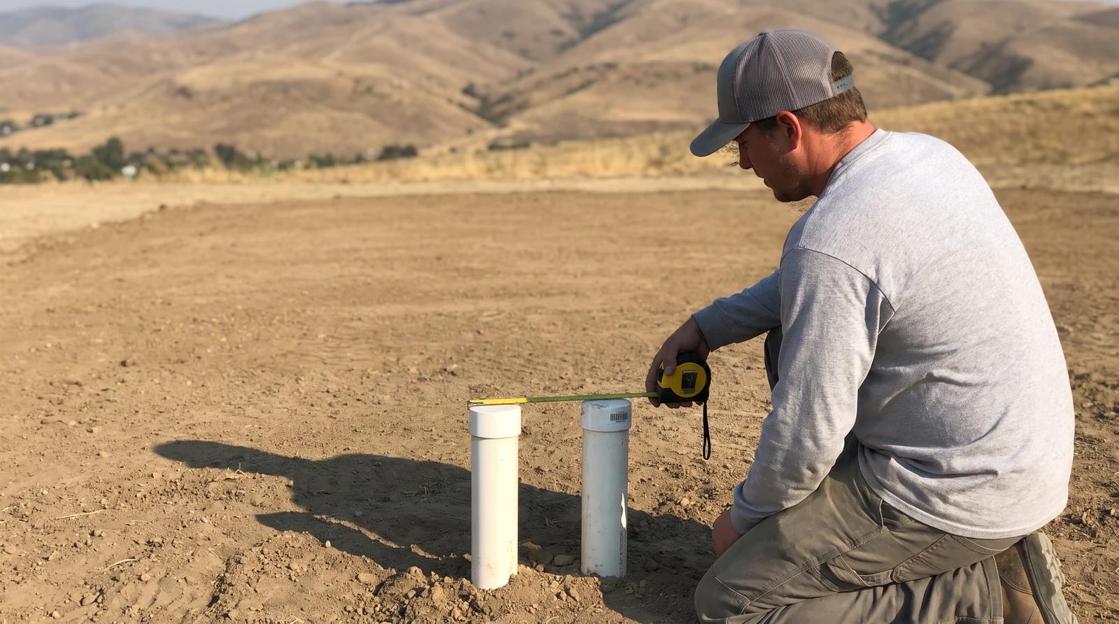 Cleared mobile home lot in Eagle, Idaho with capped utility stubs and a worker measuring before a new manufactured home is set