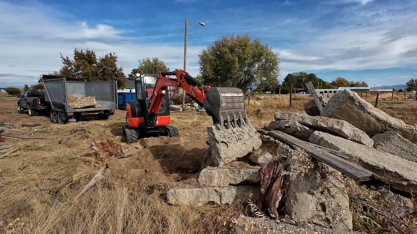 Excavator breaking up and removing concrete at a rural property near Boise Idaho