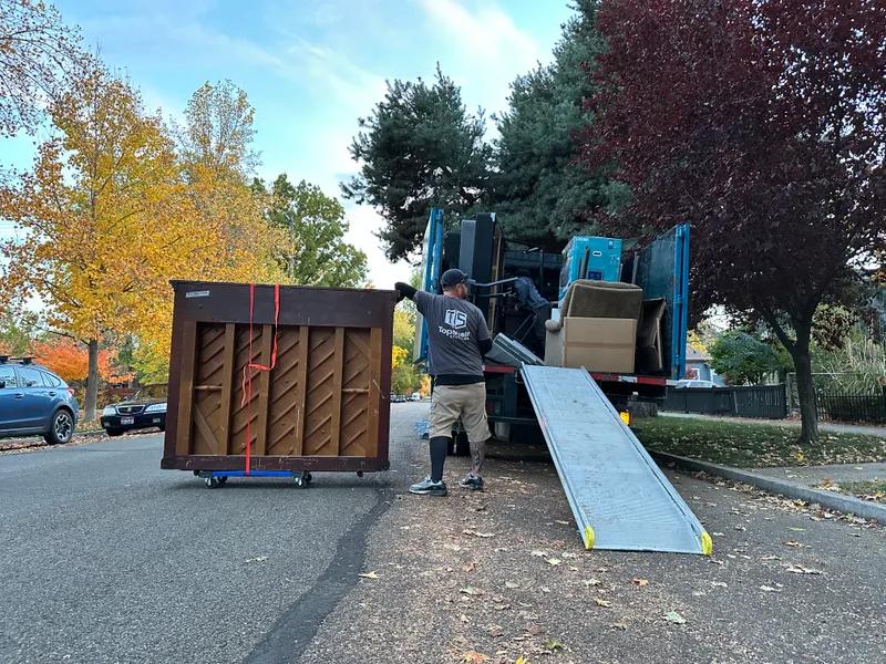 Top Shelf crew member guiding a tipped piano on a dolly up the truck ramp during a removal in Boise Idaho