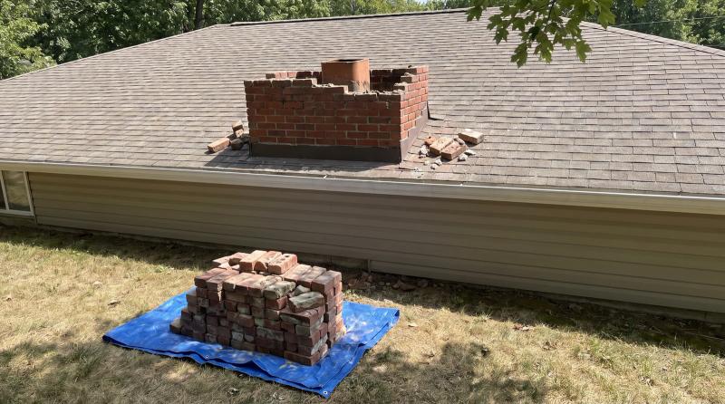 Old red brick chimney partly taken down on a Boise, Idaho home's roof, with salvaged bricks stacked on a tarp in the yard below