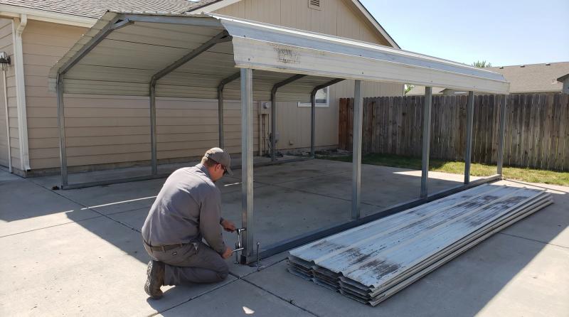 Worker taking apart an old metal carport frame on a concrete pad beside a house in Boise, Idaho