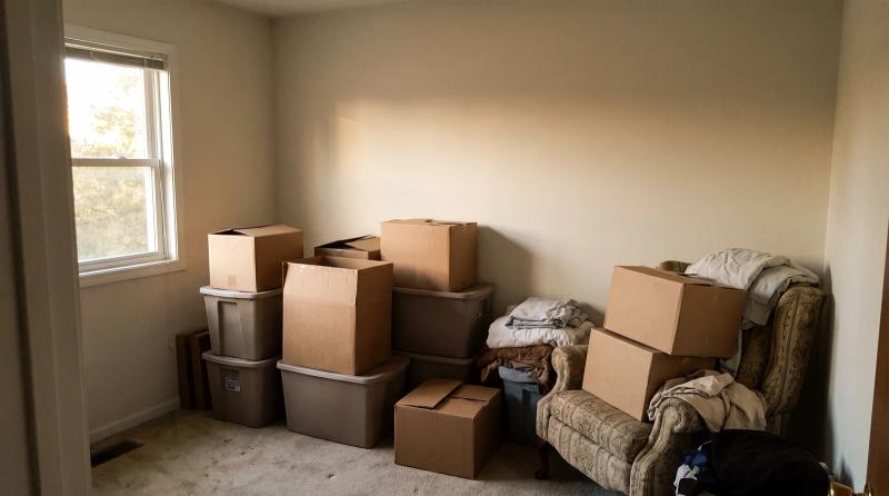 Cluttered spare bedroom with stacked boxes, plastic bins and an old armchair before a hoarder cleanout in Eagle, Idaho