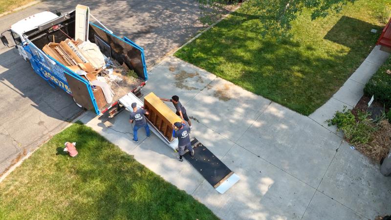 Aerial view of three Top Shelf crew members in branded shirts loading an upright piano up the ramp into the junk removal truck at a residential property in Meridian Idaho