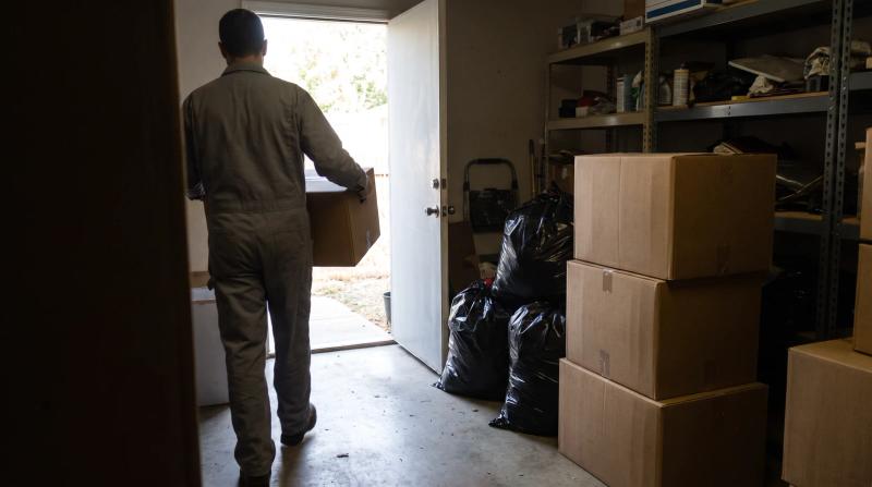 Crew member carrying a box past metal shelving to clear a back exit during a commercial hoarding cleanup in Star, Idaho