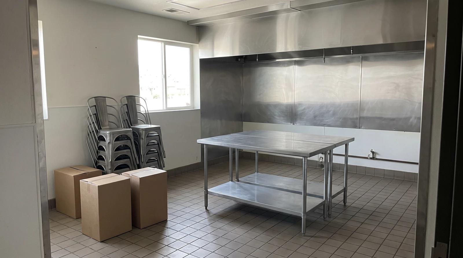 Empty restaurant kitchen with a bare stainless steel prep table, stacked chairs and boxes during a commercial property cleanout in Boise, Idaho