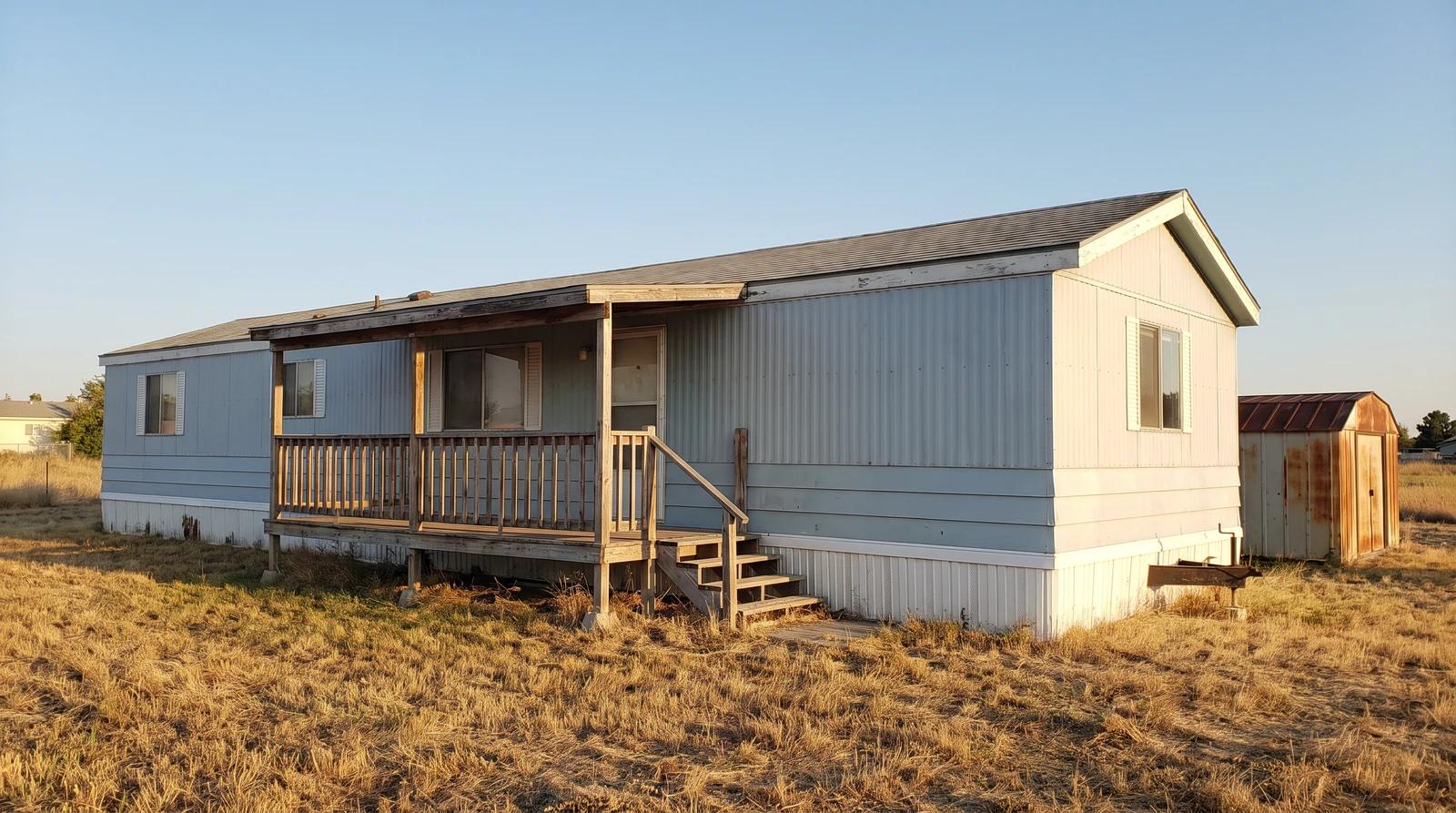Older single-wide mobile home with a worn porch on an inherited rural lot in Nampa, Idaho, waiting for removal