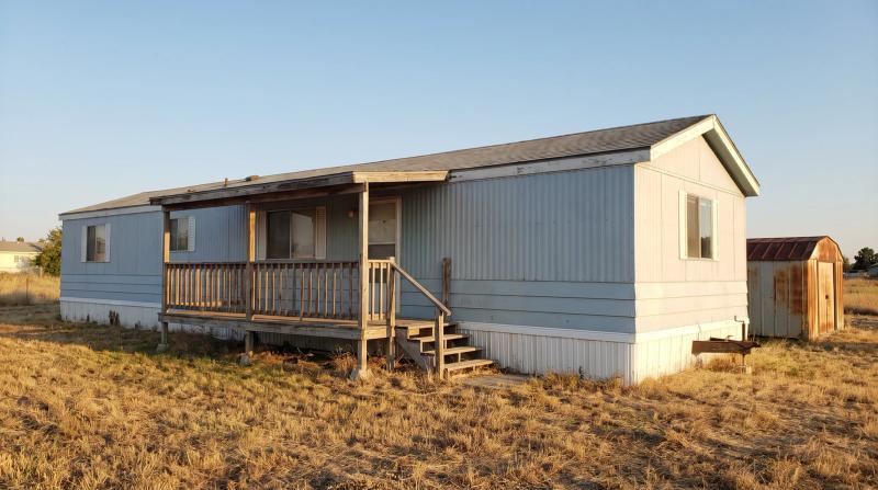 Older single-wide mobile home with a worn porch on an inherited rural lot in Nampa, Idaho, waiting for removal