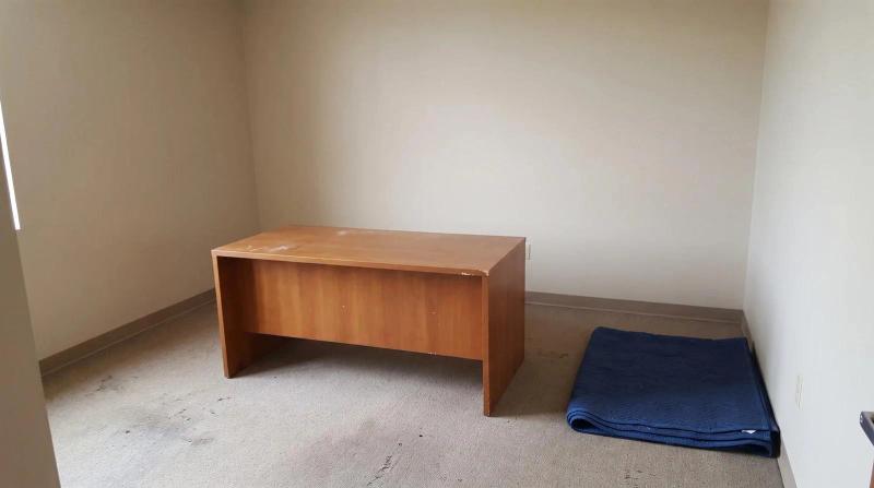 An emptied office suite in Nampa, Idaho with bare walls, one wooden desk left behind and a folded moving blanket on the floor