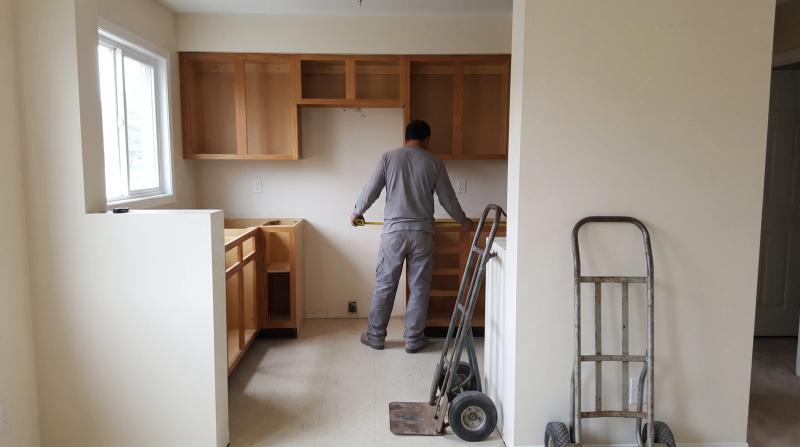 Empty kitchen during a remodel in Boise, Idaho, after the old appliances were removed, with a hand truck and a worker measuring the open space