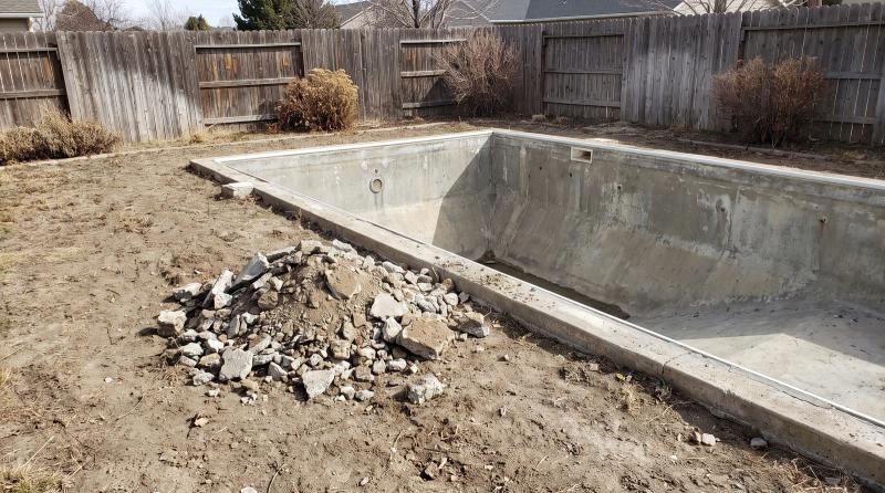 Empty concrete pool shell with broken concrete stacked beside it during a pool demolition in a Boise, Idaho backyard