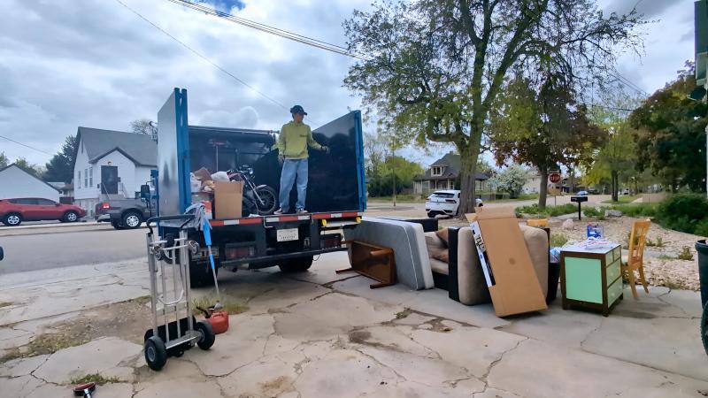 Top Shelf crew member standing in the truck bed with a motorcycle loaded alongside furniture and junk during a curbside removal in Boise Idaho