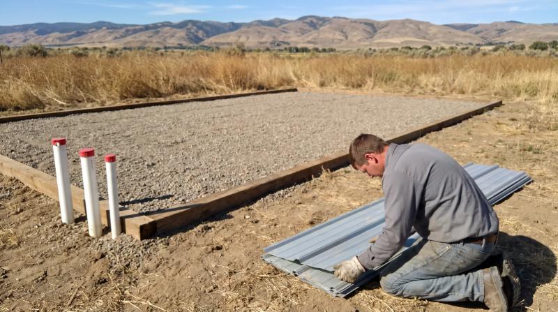 Worker stacking old metal skirting panels next to a cleared mobile home pad in a park in Meridian, Idaho