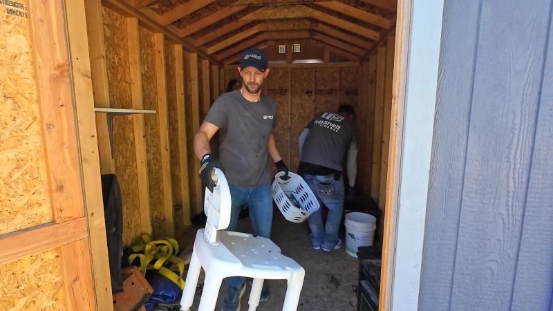 Two Top Shelf crew members in branded shirts clearing out a storage shed carrying chairs and household items in Eagle Idaho