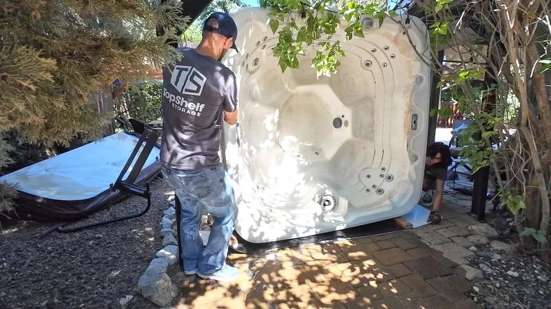 Top Shelf crew member tipping a hot tub on its side for removal from a backyard patio in Caldwell Idaho