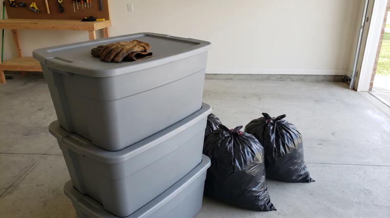 Lidded storage bins, bagged trash, and work gloves on a clean concrete floor after a garage cleanout in Nampa, Idaho