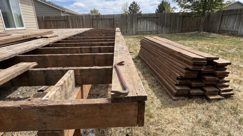 Partly removed wooden deck with exposed joists and stacked old boards in a Nampa, Idaho backyard