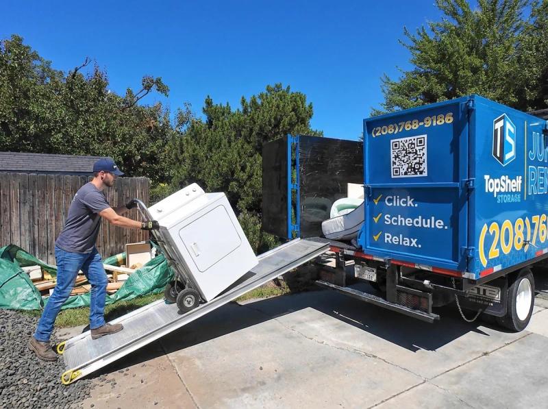Top Shelf crew member loading a clothes dryer up the ramp into the branded junk removal truck in Boise Idaho