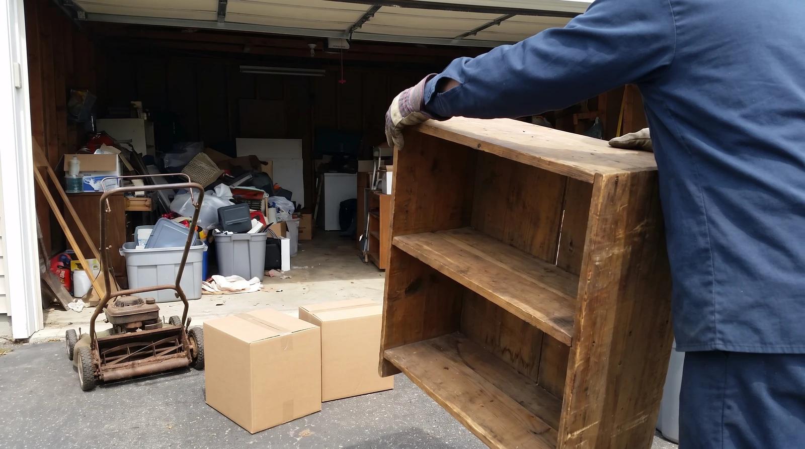 Worker carrying old shelving out of a cluttered rental garage during a property cleanout in Meridian, Idaho