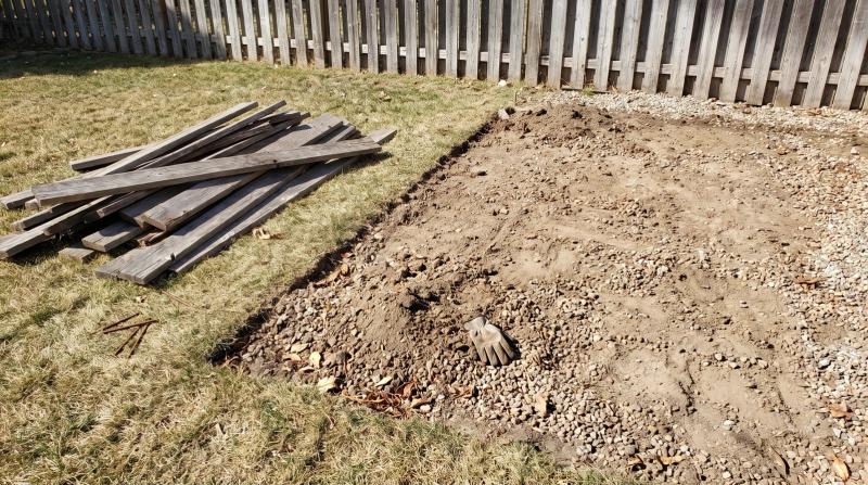 Bare dirt and gravel where a backyard deck once stood in Garden City, Idaho, with a stack of removed deck boards on the grass beside it
