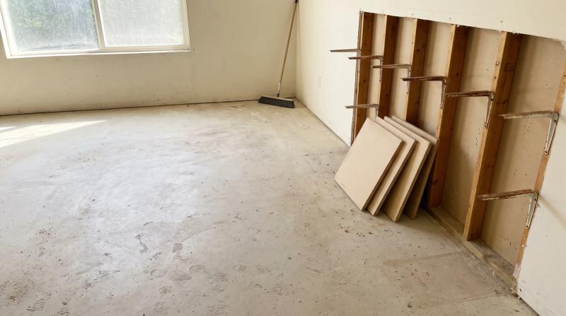Emptied garage in Garden City, Idaho with bare concrete floor, leftover shelf brackets on the studs, and stacked particleboard shelf boards after a garage cleanout