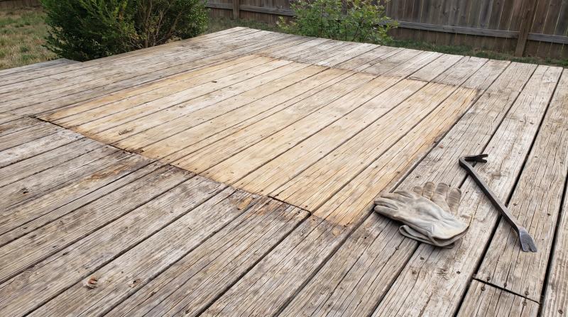 Wooden deck in Emmett, Idaho showing the lighter rectangle of boards left behind after a hot tub was removed, with work gloves and a pry bar nearby