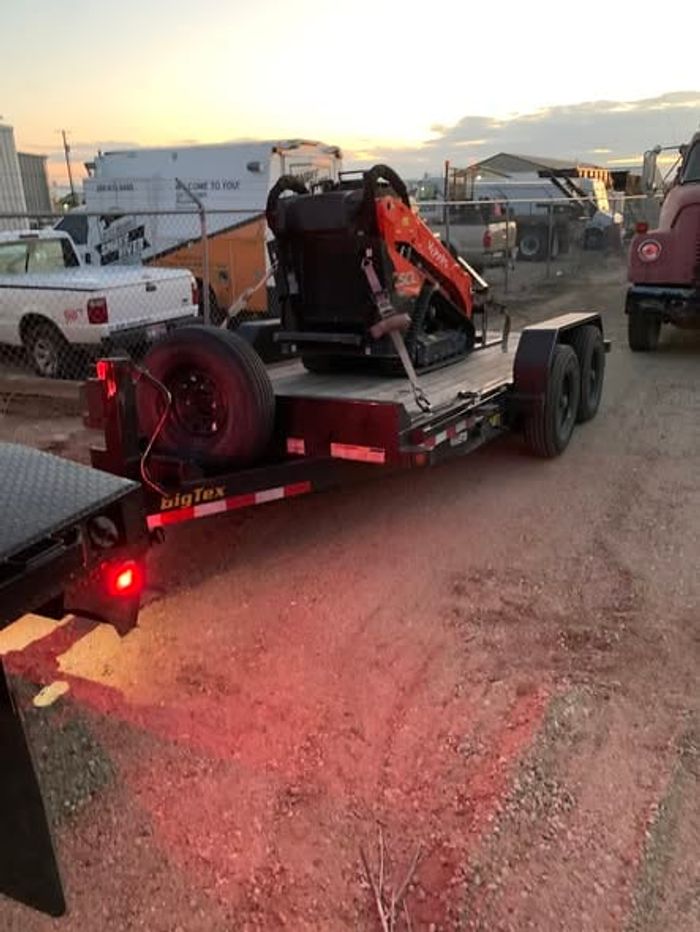A skid steer strapped to a trailer under the lights at night