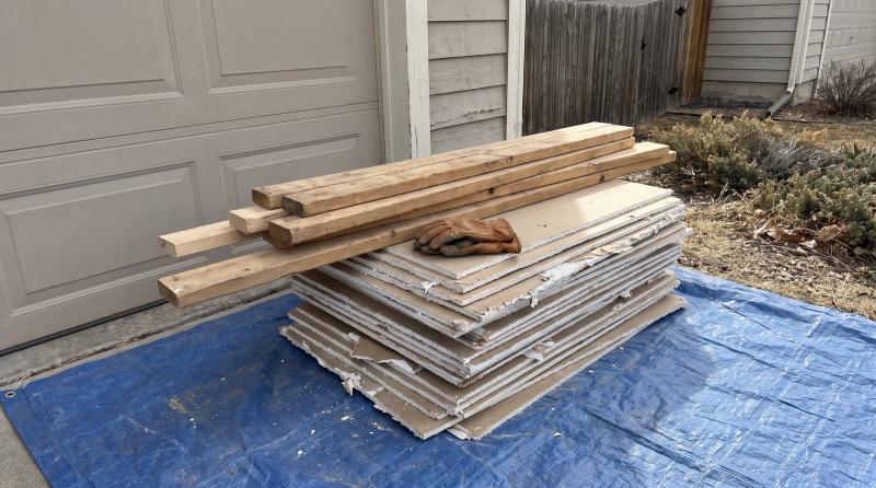 Sorted DIY remodel debris of drywall and lumber on a tarp beside a home garage in Middleton, Idaho