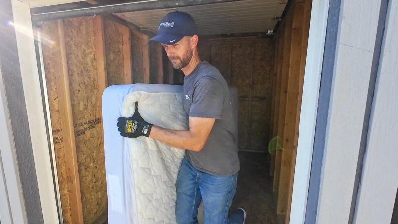 Top Shelf crew member carrying a mattress out through the doorway of a shed during a cleanout job in Nampa Idaho