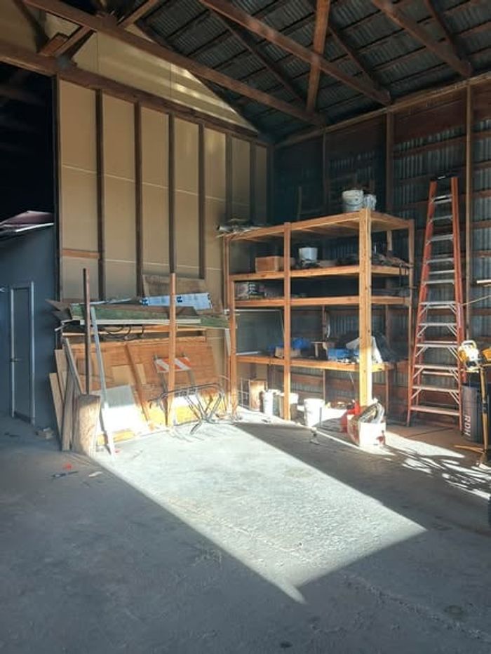 A shop building partway through a cleanout, floor mostly cleared, shelving still standing