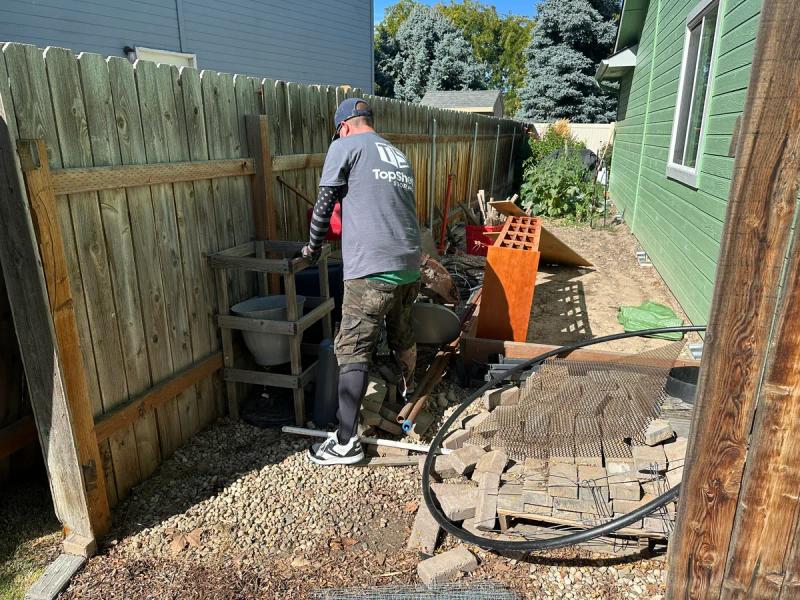 Top Shelf crew member clearing stacked bricks pavers and miscellaneous debris from a backyard side yard in Nampa Idaho