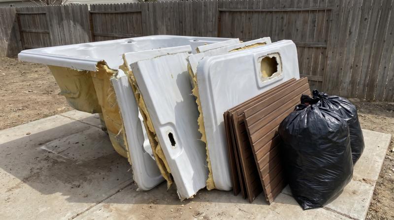 Cut-up hot tub shell sections and wooden cabinet panels stacked on a backyard patio in Boise, Idaho, ready for removal