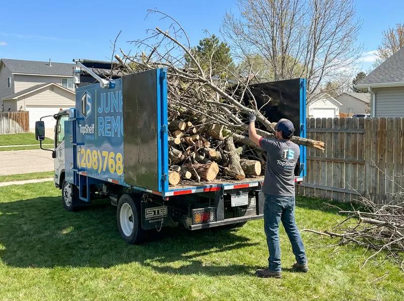 Top Shelf crew member loading cut tree branches into the branded truck packed full of logs and limbs at a residential property in Meridian Idaho