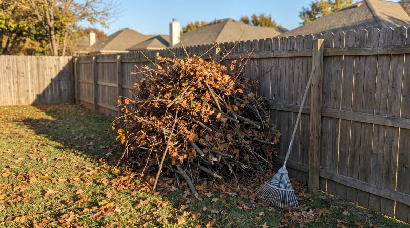 Pile of pruned branches and fall leaves beside a wooden fence, waiting for yard debris removal in a Boise, Idaho backyard