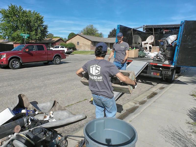 Two Top Shelf crew members loading outdoor furniture and yard debris onto the junk removal truck in a neighborhood in Emmett Idaho