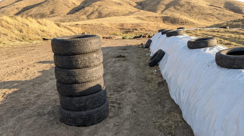 Stack of old weathered silage pile tires beside a plastic-covered bunker on a farm near Emmett, Idaho, ready for tire disposal