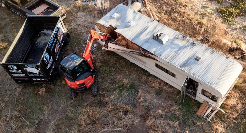 Top Shelf excavator demolishing a camper for removal