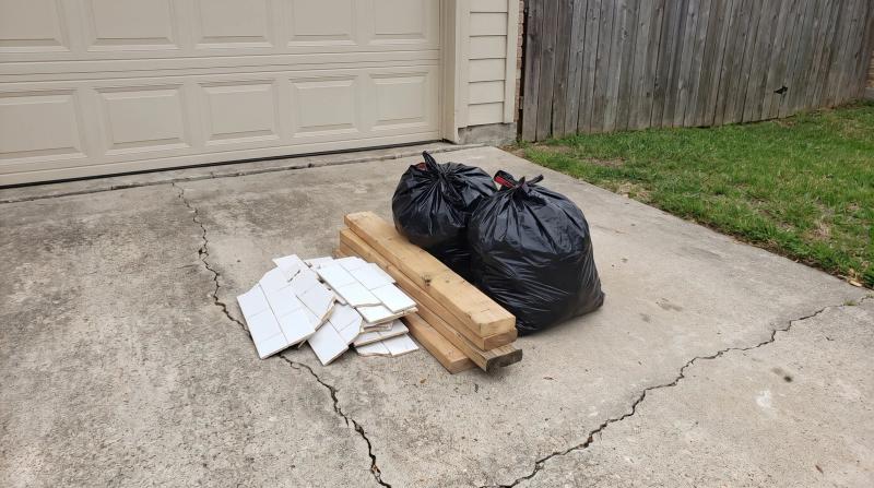 Leftover remodel debris including broken tile, cut lumber, and sealed contractor bags stacked on a driveway at a home in Boise, Idaho, waiting for construction cleanup