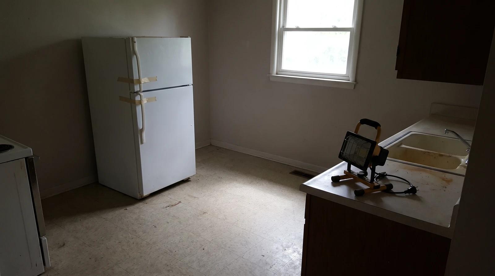Taped-shut refrigerator in the dim kitchen of an empty foreclosed home in Kuna, Idaho, ready for a property cleanout