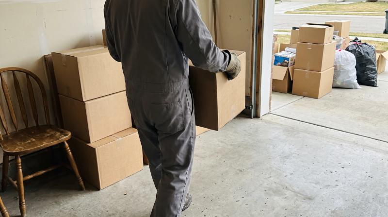 Worker carrying a box out of a cluttered garage during a one-room hoarding cleanup in Meridian, Idaho
