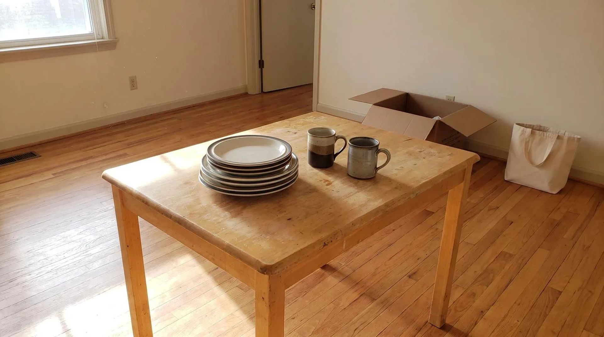 Mismatched dinner plates and coffee mugs left on a bare kitchen table in an empty home during an estate cleanout in Nampa, Idaho