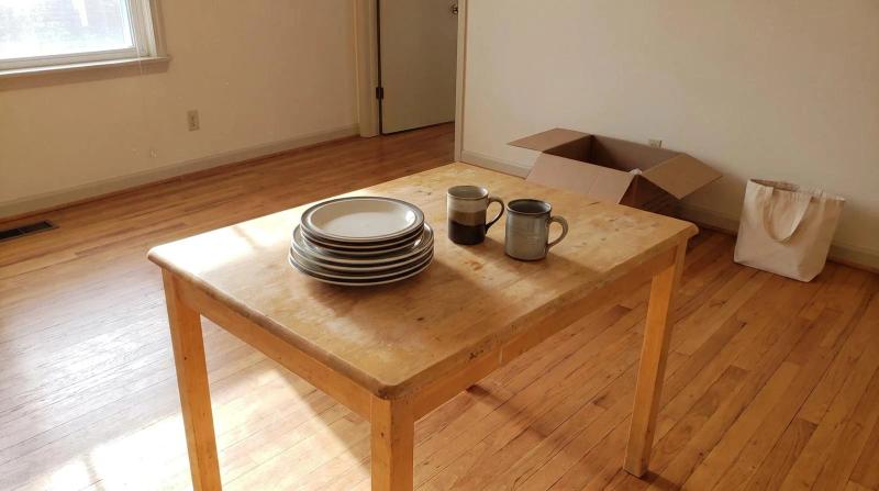 Mismatched dinner plates and coffee mugs left on a bare kitchen table in an empty home during an estate cleanout in Nampa, Idaho