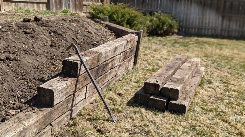 Half-removed railroad tie retaining wall with loose timbers and exposed soil in a backyard in Boise, Idaho