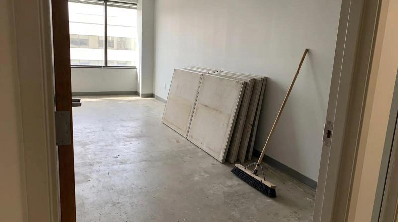 Empty commercial office suite in Boise, Idaho with stacked gray cubicle panels and a push broom against a bare wall