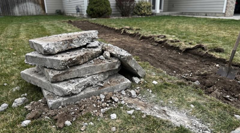 Stacked pieces of broken driveway concrete on a residential lawn beside bare dirt after a concrete removal job in Boise, Idaho.