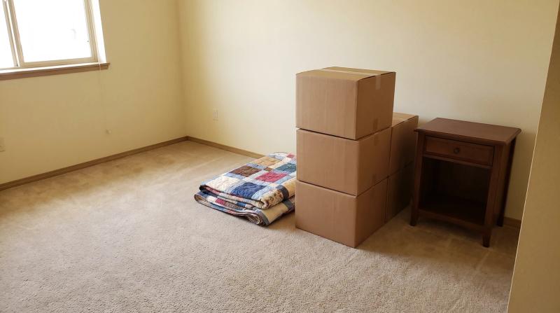 Packed boxes, a folded quilt, and a wooden nightstand in an emptied assisted living apartment during an estate cleanout in Kuna, Idaho