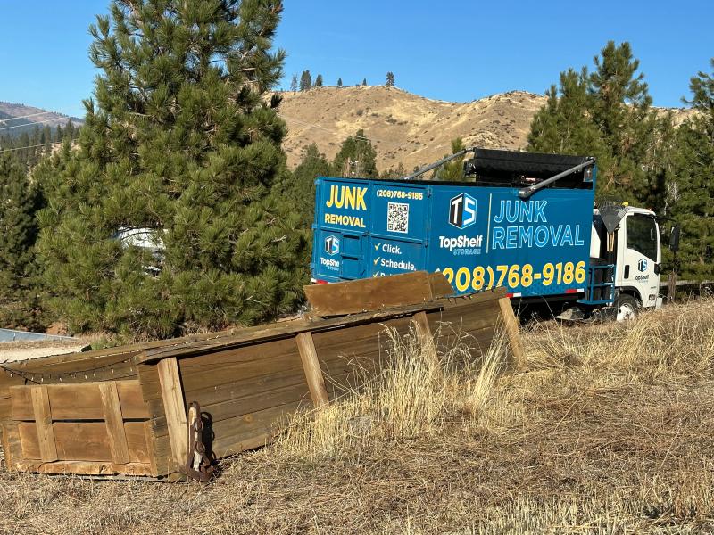 Top Shelf branded junk removal truck on a rural property with old wooden fence and farm debris ready for removal in Caldwell Idaho