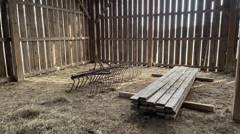 Sunlit interior of an old wooden barn with loose hay, a rusted farm implement and stacked lumber, waiting for a barn cleanout near Nampa, Idaho