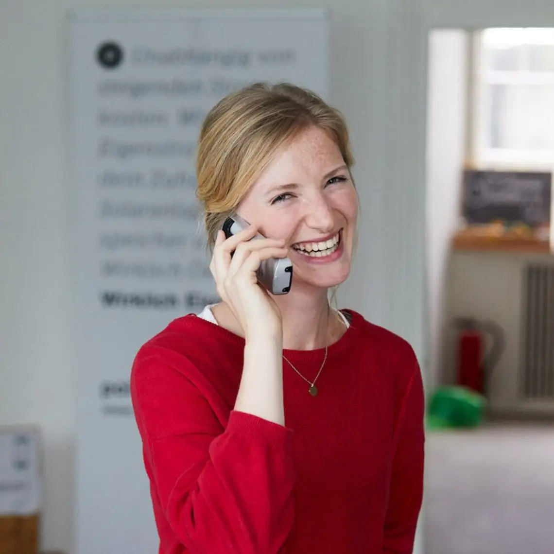 Eine Polarstern Energie Mitarbeiterin steht im Büro und hält ein Telefon am Ohr, während sie in die Kamera lacht