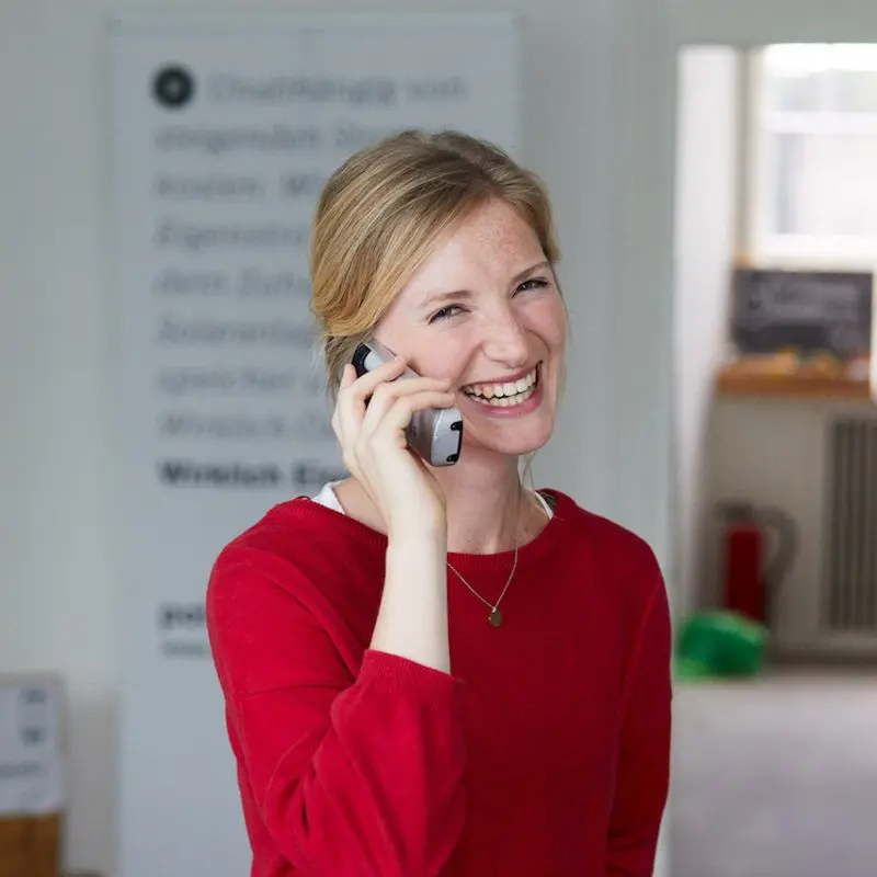 Eine Polarstern Energie Mitarbeiterin steht im Büro und hält ein Telefon am Ohr, während sie in die Kamera lacht