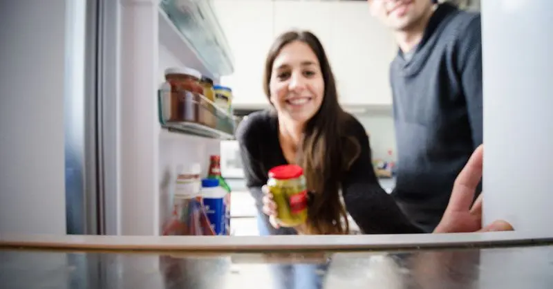 Frau hält Glas in der Hand und schaut in Kühlschrank